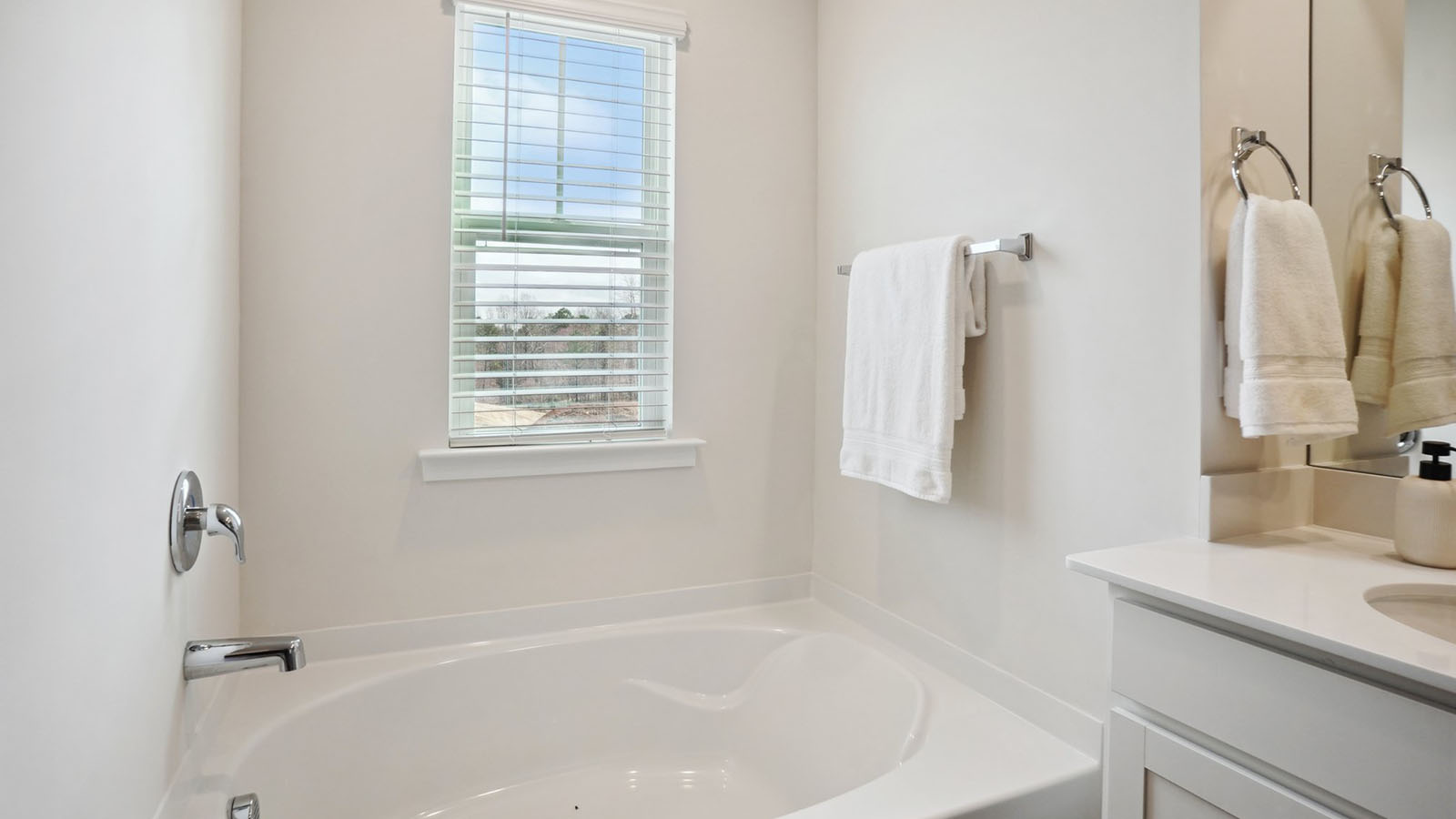 Model primary bathroom with white cabinets and counters, double sinks, and glass door shower