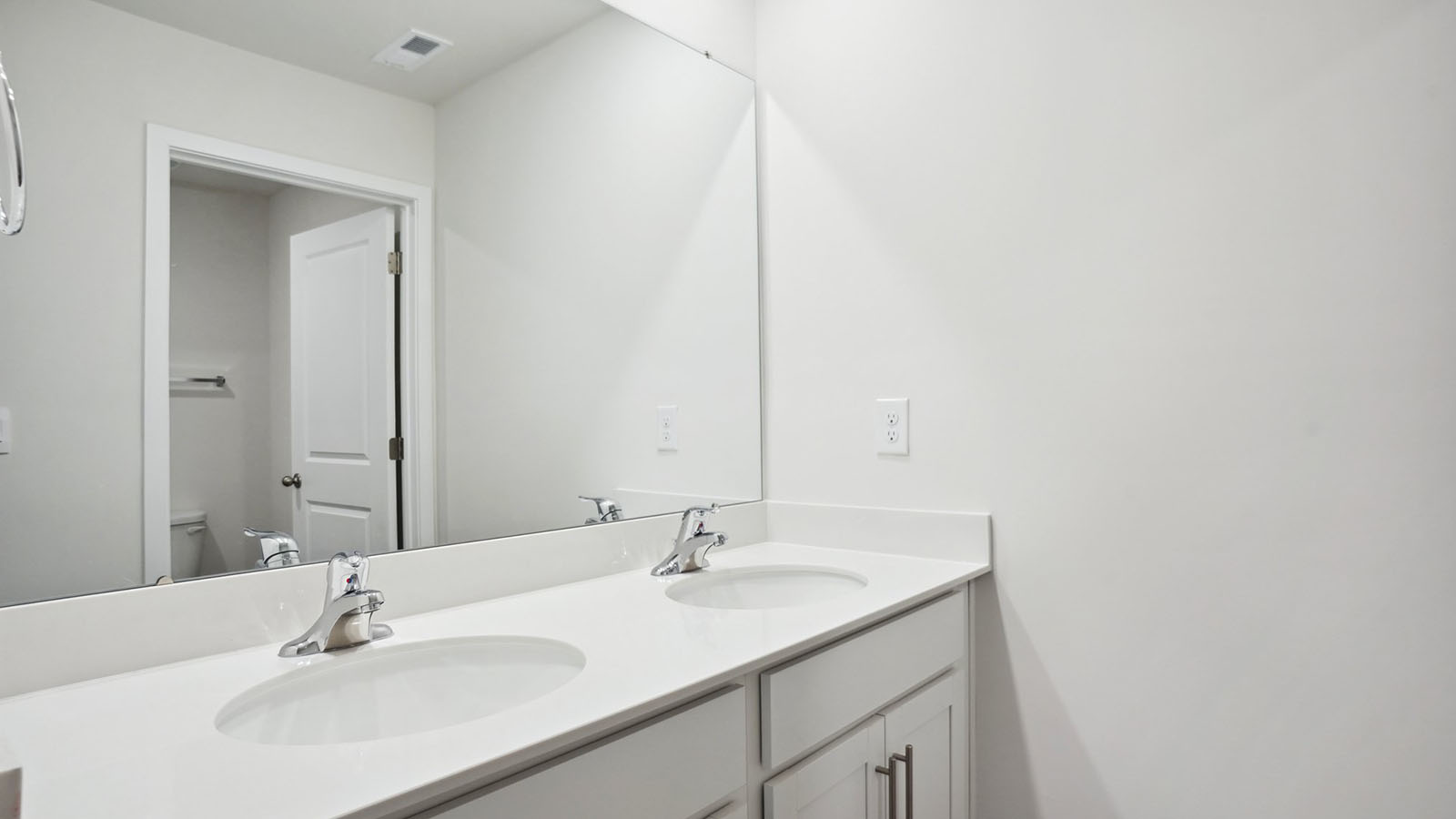 Model bathroom with white counters and cabinets, double sinks and glass door shower