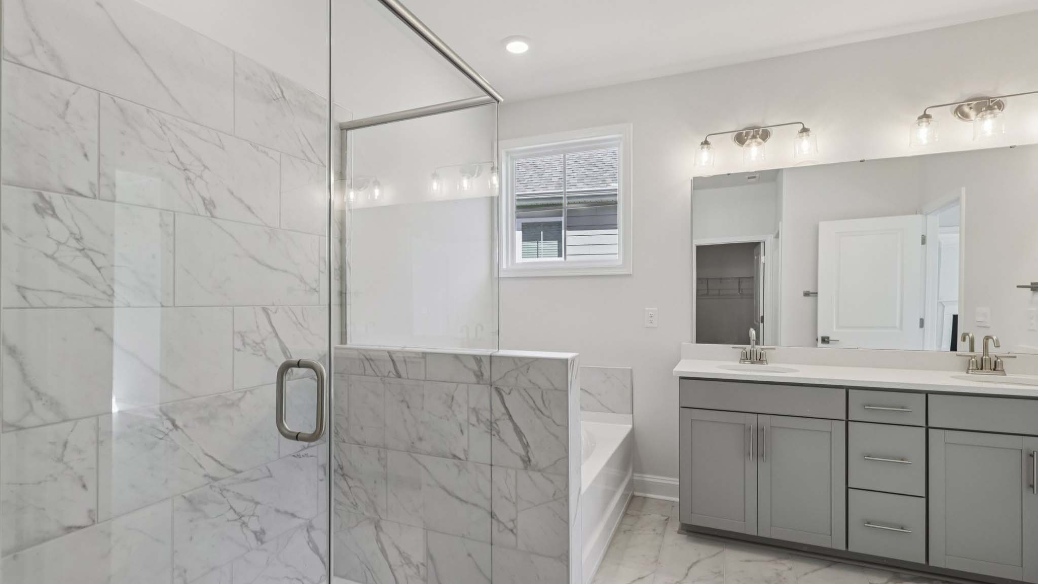 primary bathroom with double sink vanity and large glass shower and bathtub