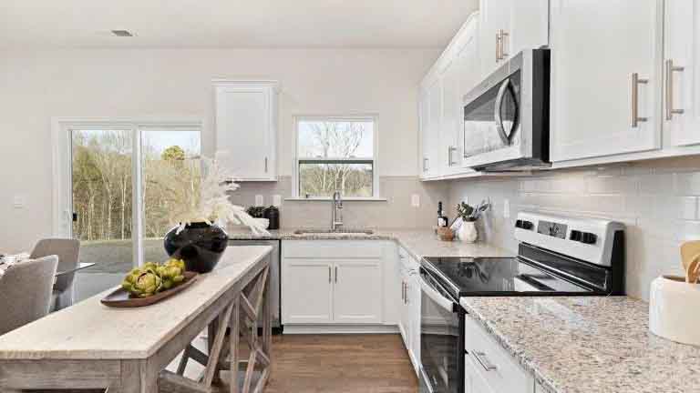 Kitchen and island with white cabinets, tile backsplash and stainless steel appliances