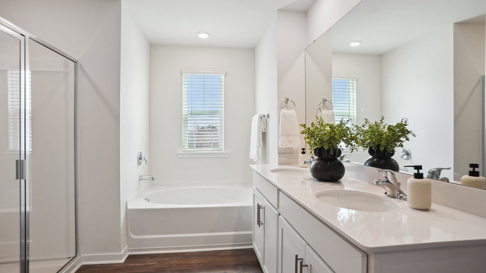 Model primary bathroom with white cabinets and counters, double sinks, and glass door shower