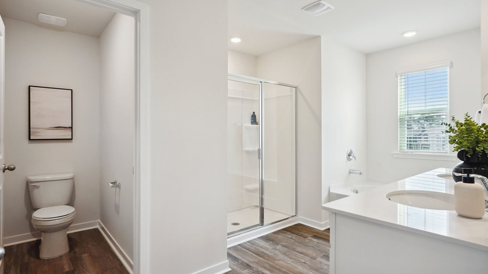 Model primary bathroom with white cabinets and counters, double sinks, and glass door shower
