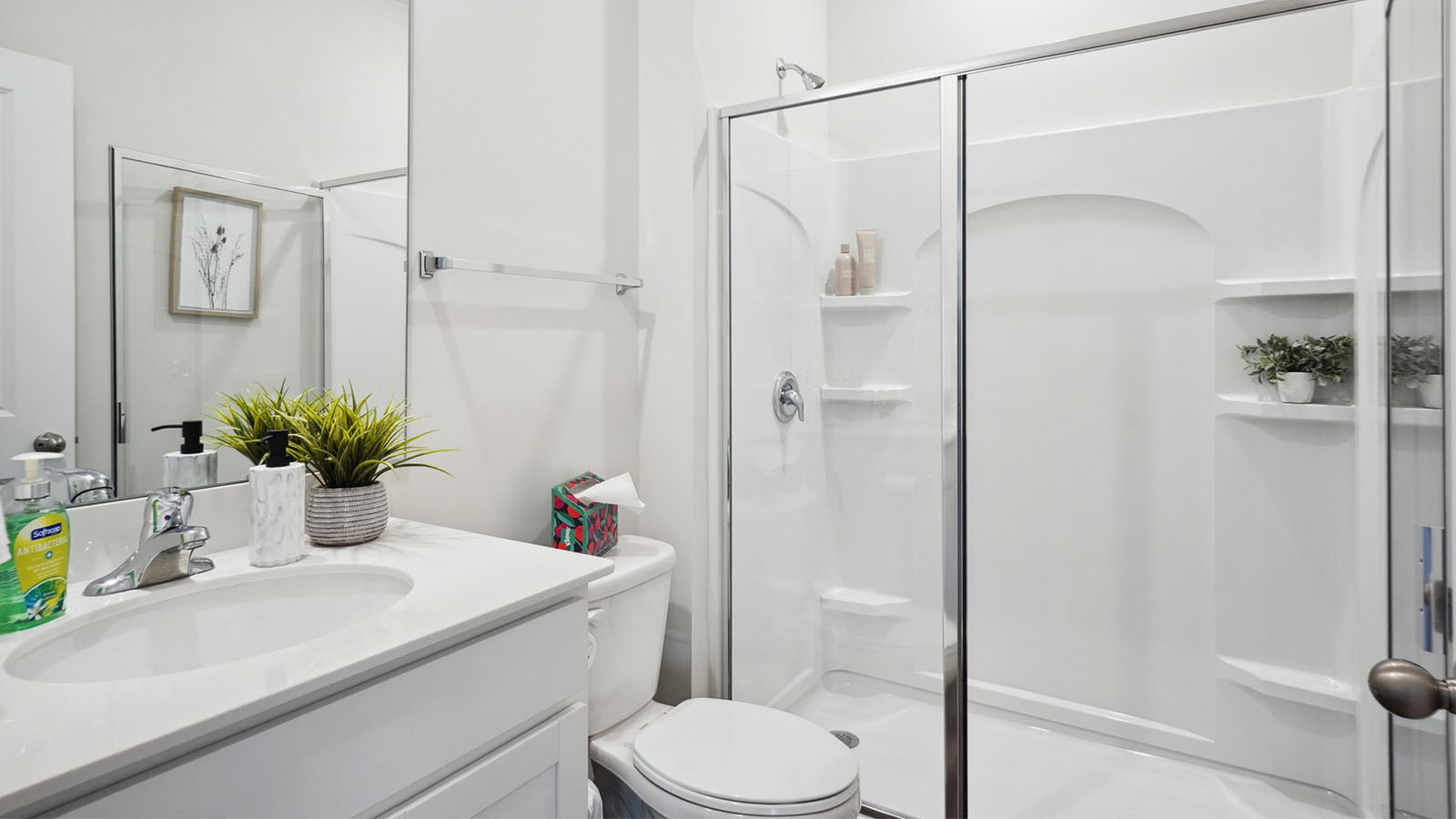 Model bathroom with white counters and cabinets, double sinks and glass door shower