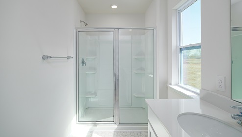 Bathroom with white counters and cabinets, and glass door standing shower