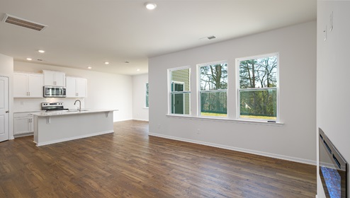 Living room space with wood floors, three large windows and view of kitchen