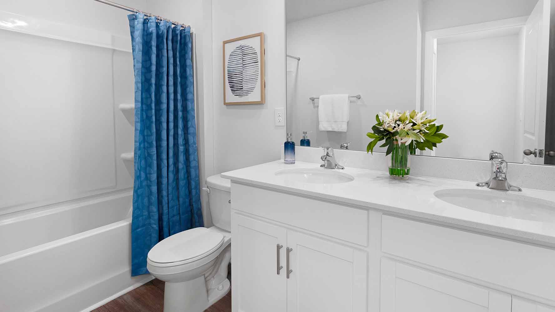Bathroom with double sinks, white counters, cabinets and glass door shower