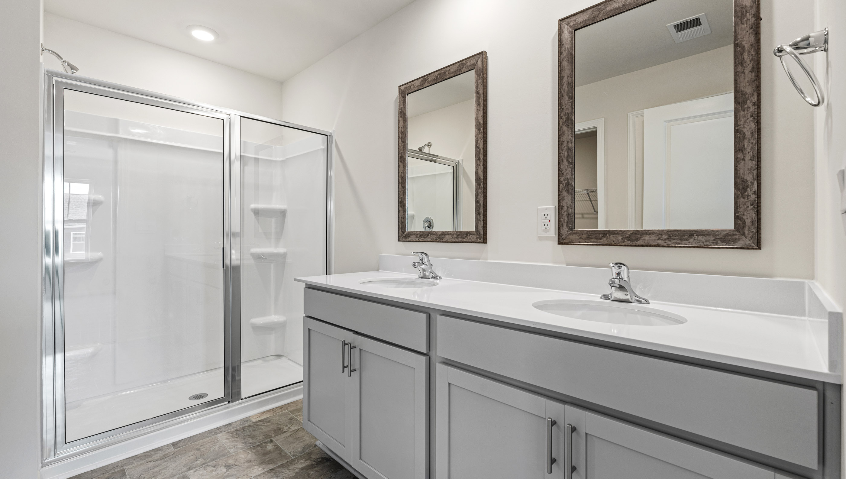 Bathroom with double sinks, white counters, cabinets and glass door shower
