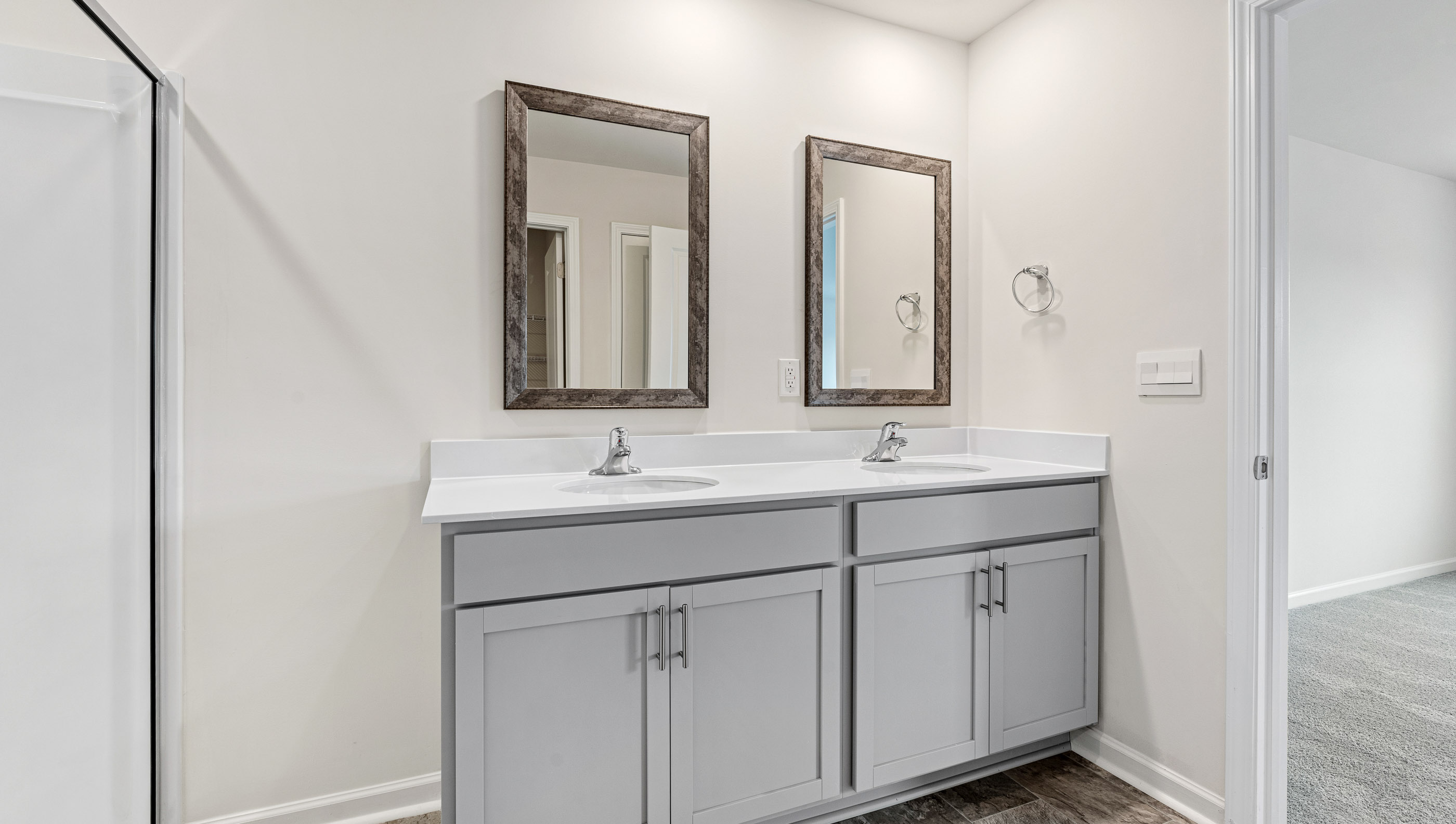 Bathroom with double sinks, white counters, cabinets and glass door shower
