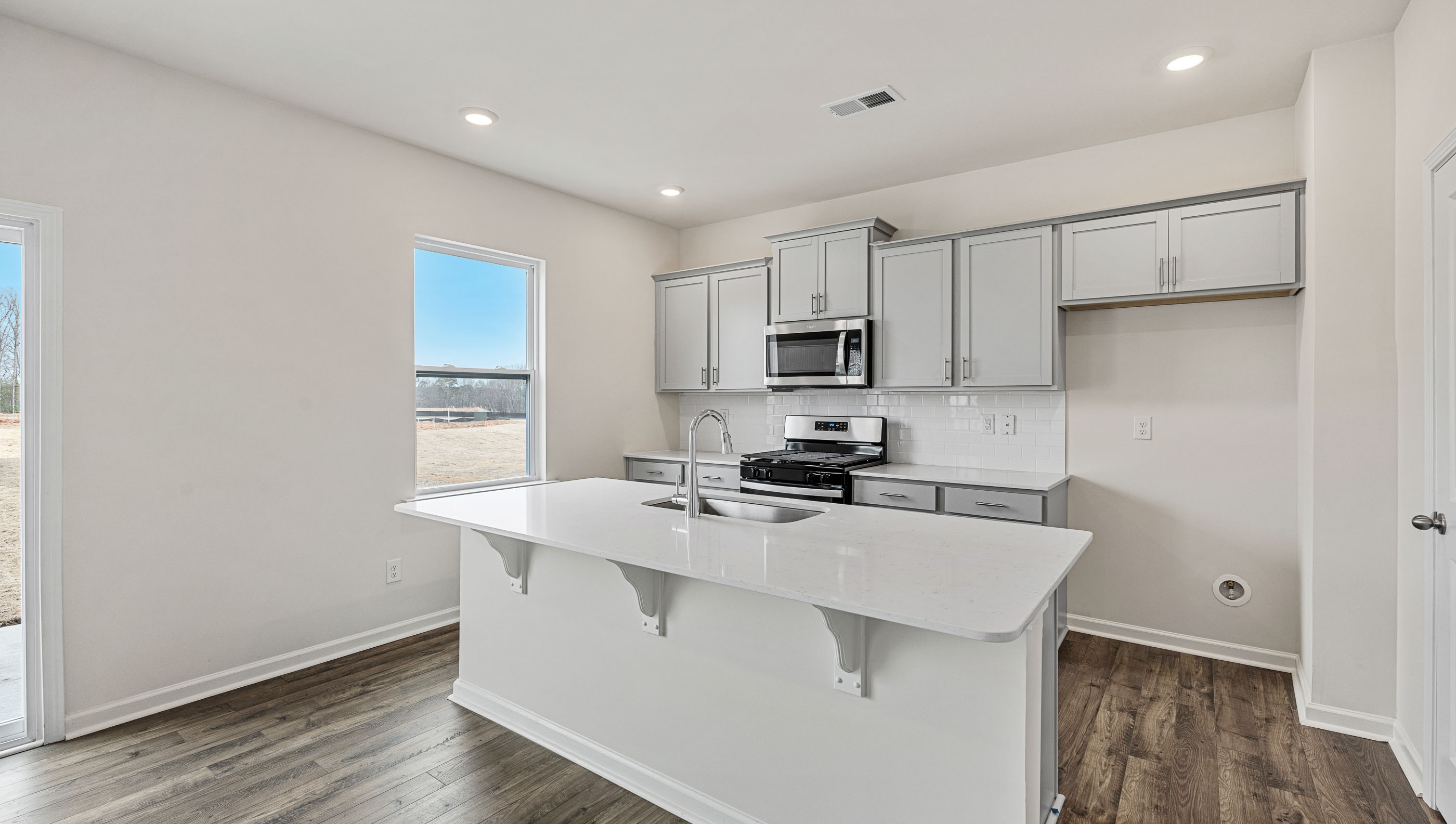 Kitchen and island with white cabinets and counters, wood floors and stainless steel appliances