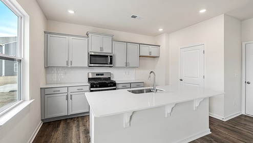 Kitchen and island with white cabinets and counters, wood floors and stainless steel appliances