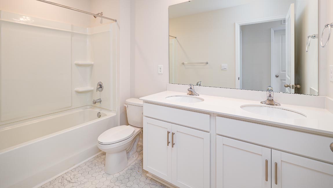 Bathroom with double sinks, white cabinets and counters, and bathtub