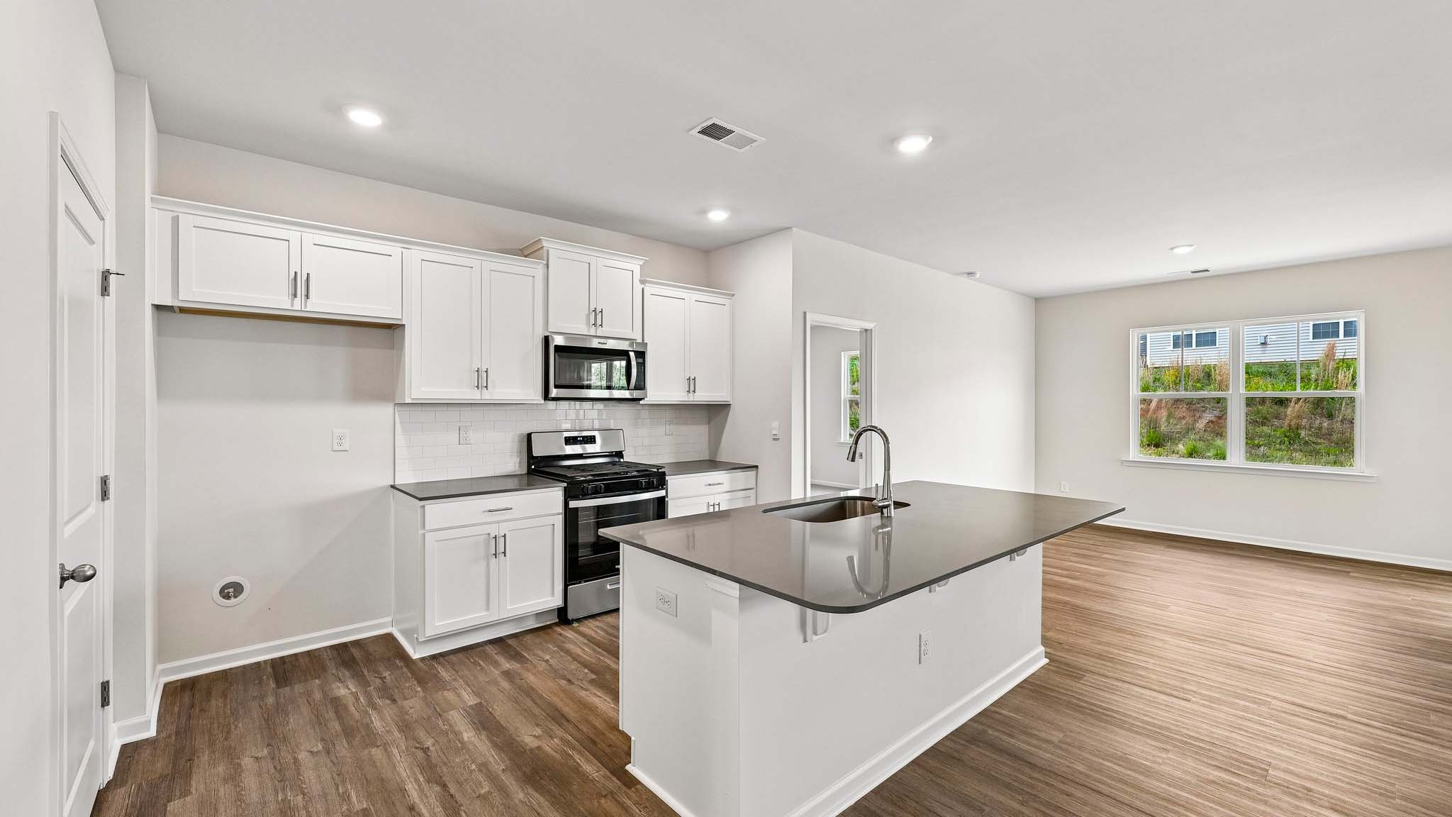 Kitchen and island with white cabinets, quarts countertops, wood floors, and stainless steel appliances