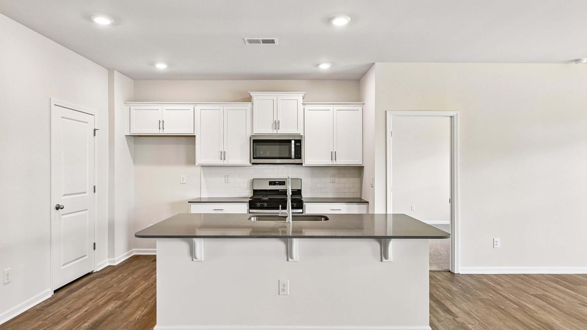 Kitchen and island with white cabinets, quarts countertops, wood floors, and stainless steel appliances