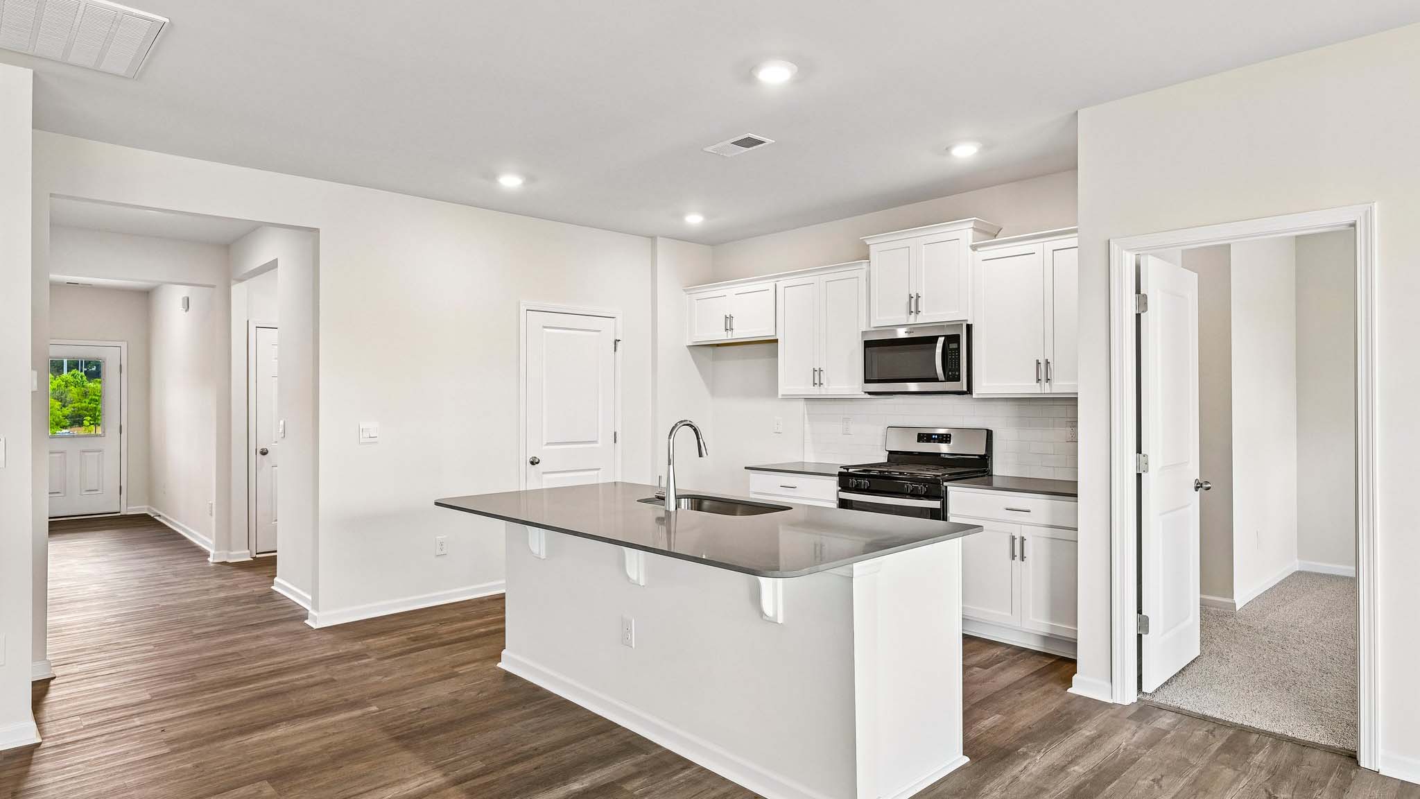 Kitchen and island with white cabinets, quarts countertops, wood floors, and stainless steel appliances