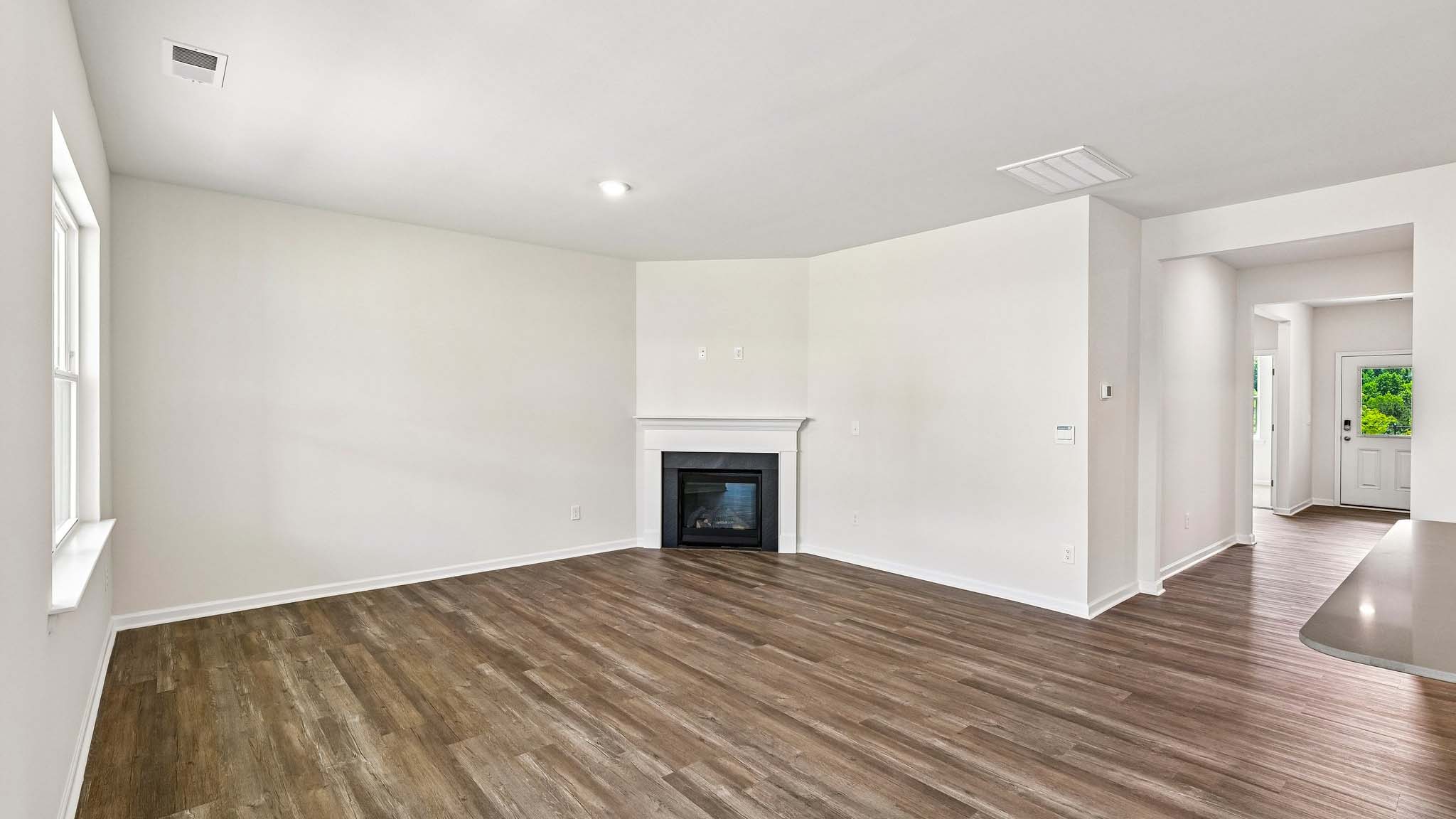 Modern open-concept living room with wood floors, and a fireplace, located beside kitchen