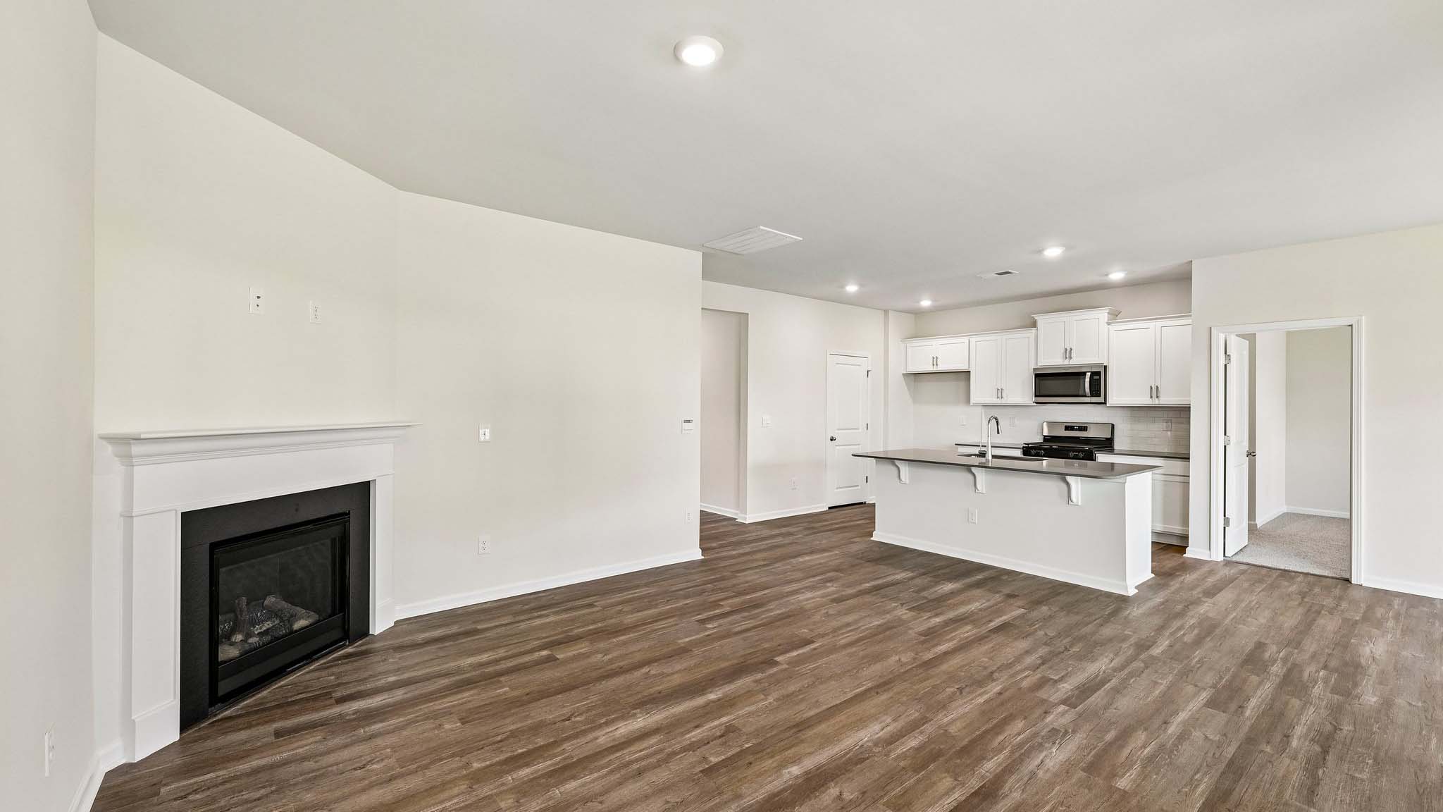 Modern open-concept living room with wood floors, and a fireplace, located beside kitchen