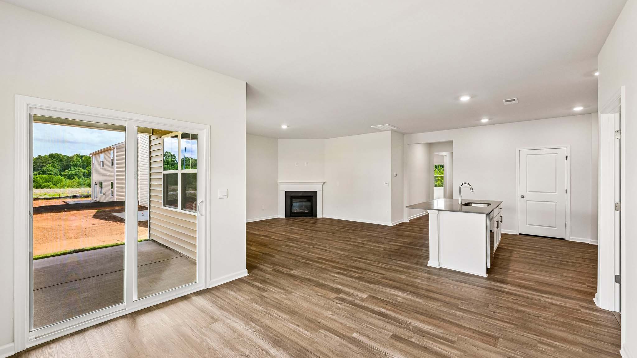 Modern open-concept living room with wood floors, and a fireplace, located beside kitchen