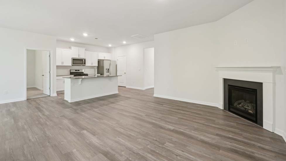 Modern open-concept living room with wood floors, and a fireplace, located beside kitchen