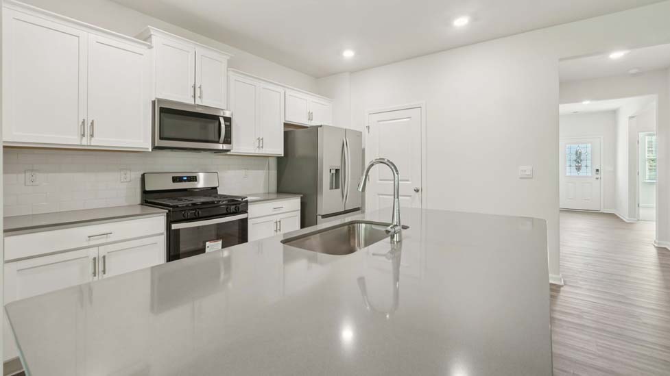 Kitchen and island with white cabinets, quarts countertops, wood floors, and stainless steel appliances