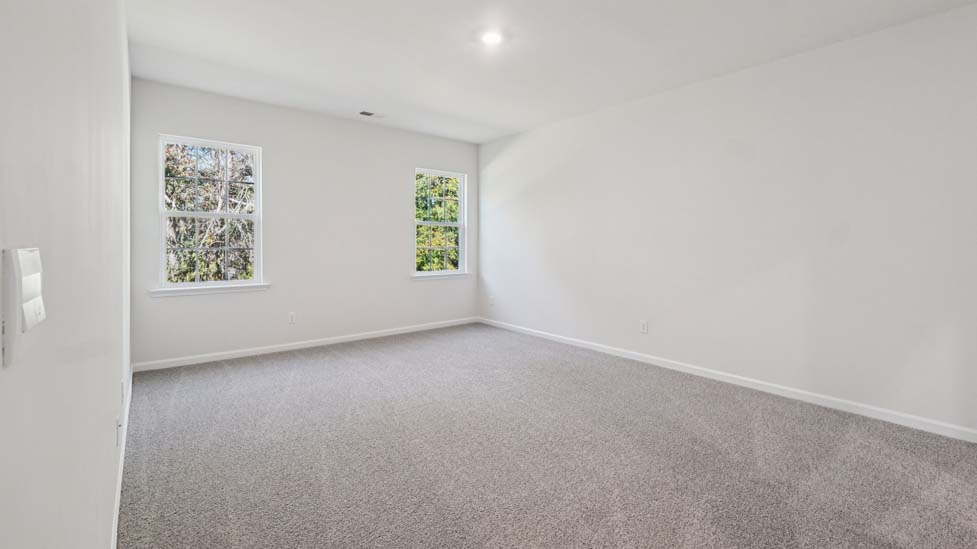 Primary bedroom with carpet and two medium sized windows