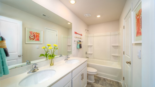 Bathroom with double sinks, bathtub, and white cabinets and counters