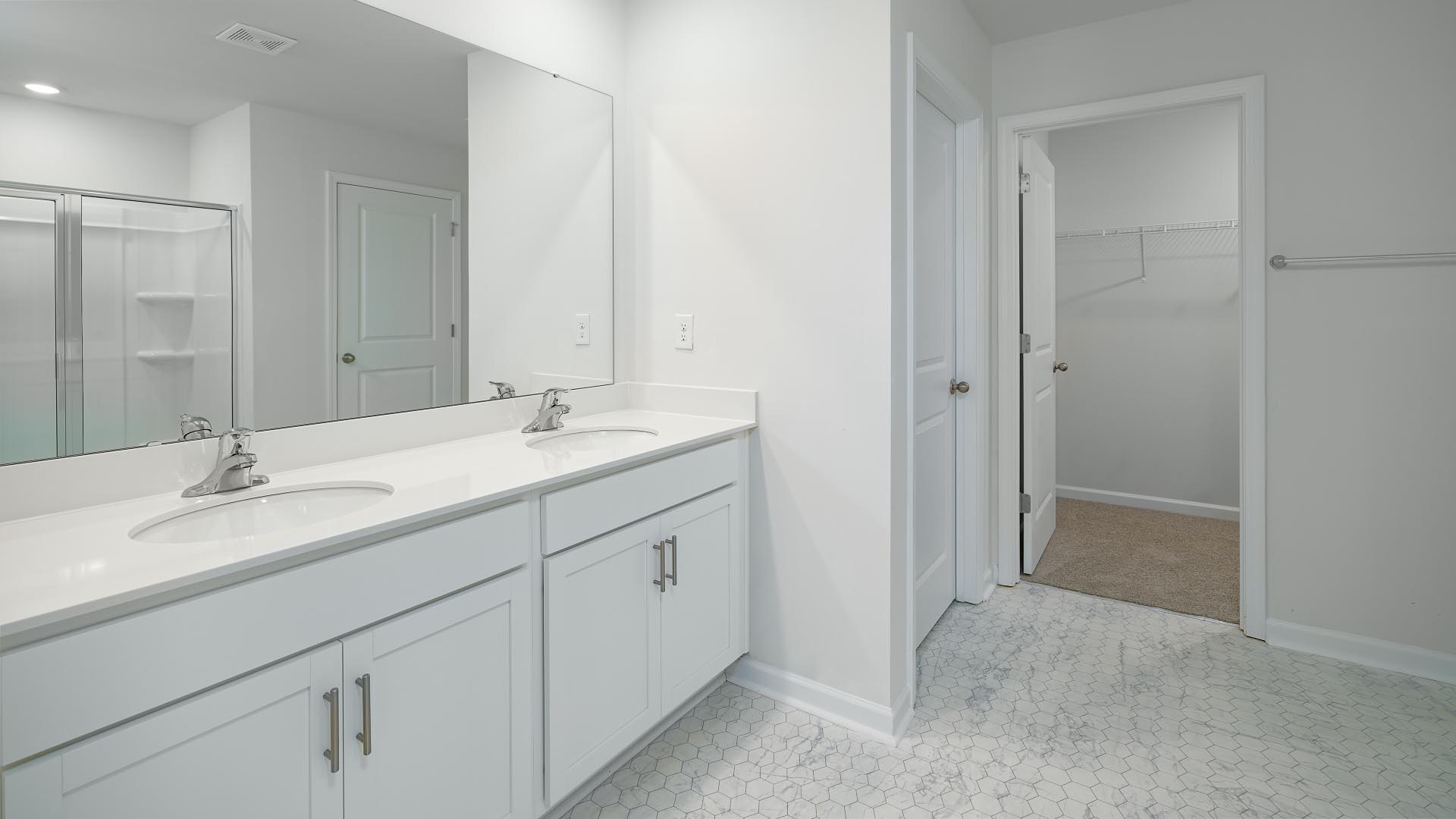 Primary bathroom with double sink vanity, white cabinets, and standing glass door shower
