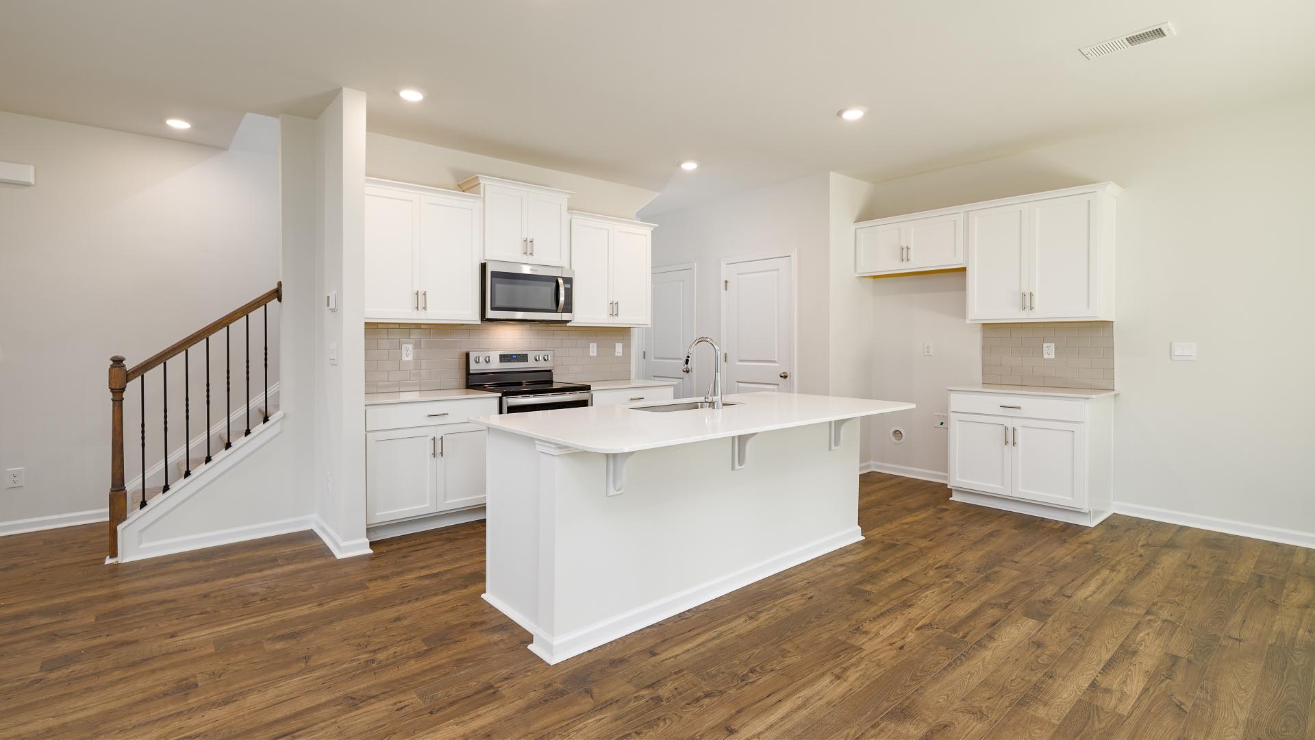 Kitchen and island with white cabinets, countertops, and stainless steel appliances