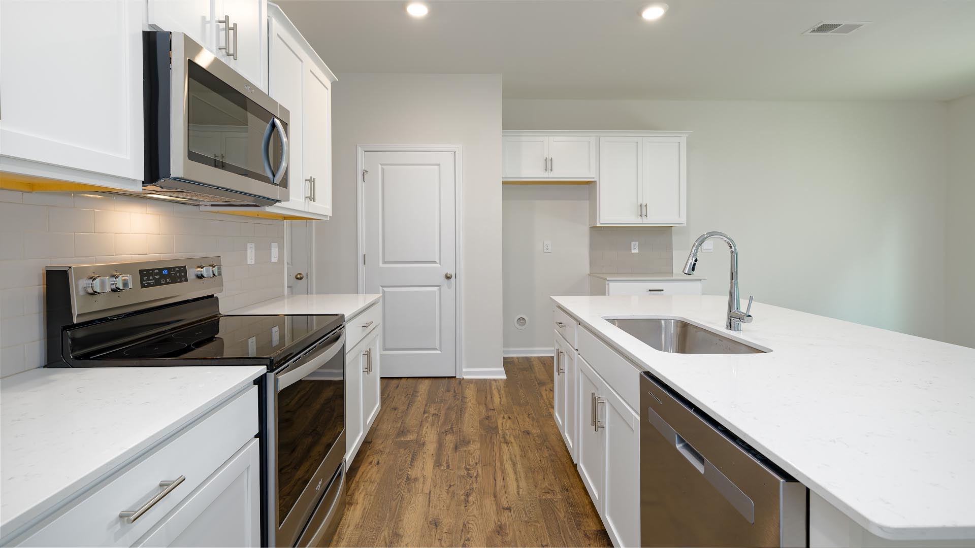 Kitchen and island with white cabinets, countertops, and stainless steel appliances