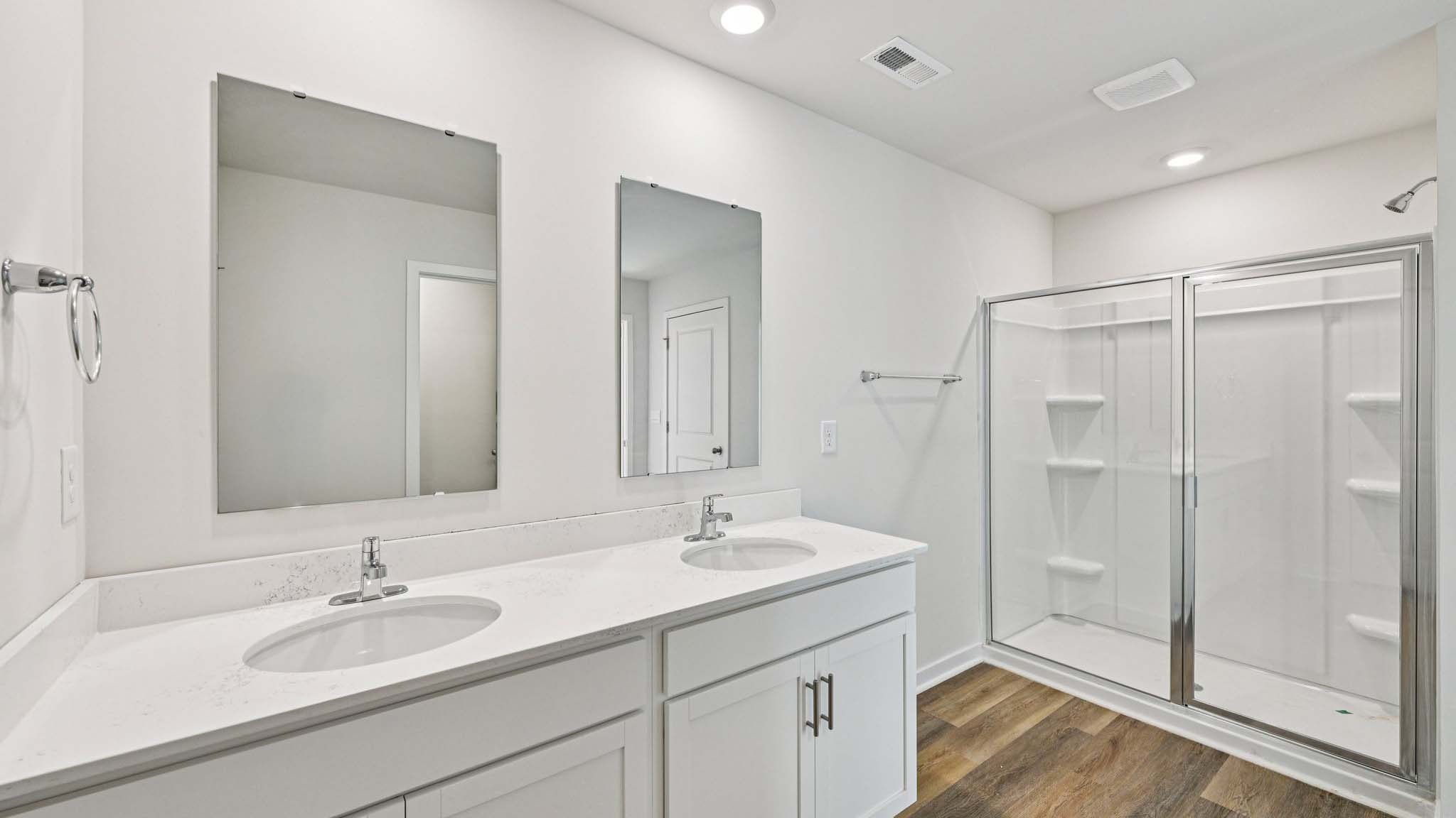 Primary bathroom with double sinks, white cabinets and glass door shower