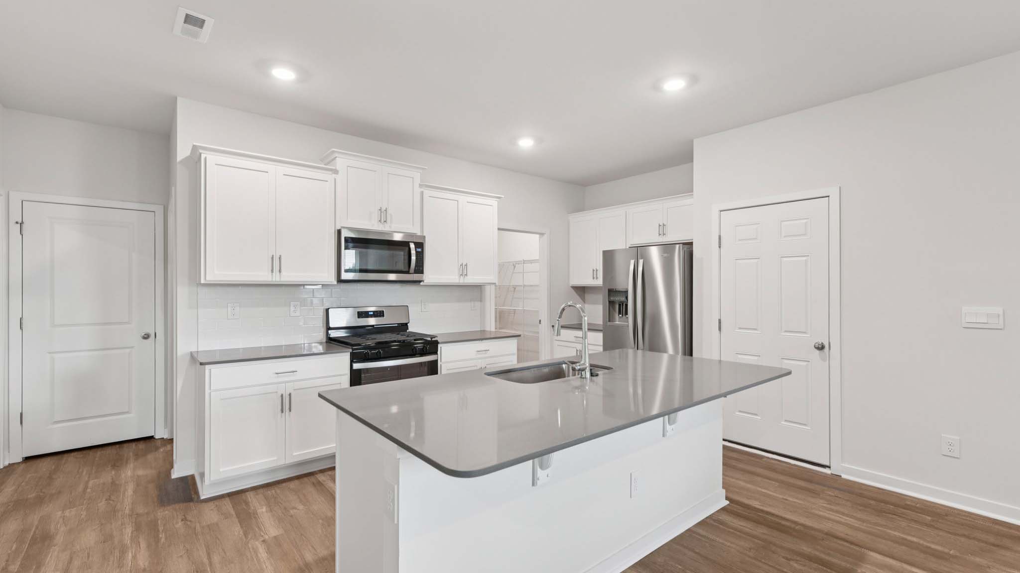 Kitchen and island with beige floors, white cabinets, white counters, and stainless steel appliances