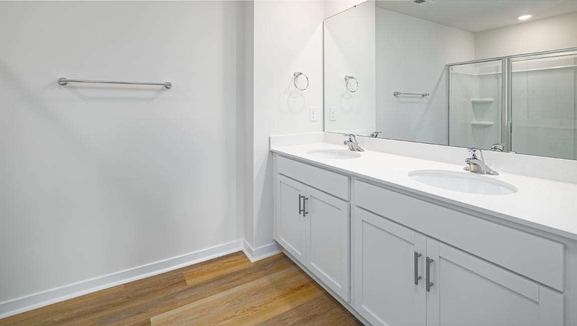 Primary bathroom with double vanity, white cabinets and standing glass door shower