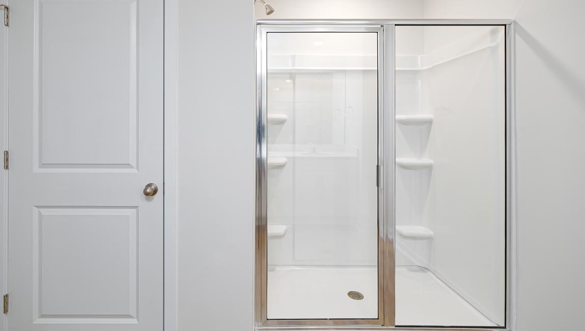 Primary bathroom with double vanity, white cabinets and standing glass door shower