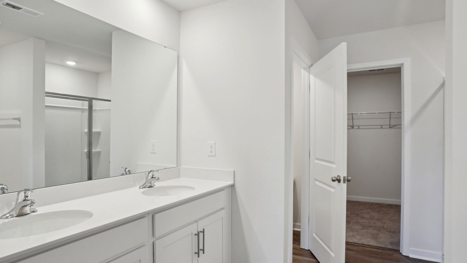 primary bathroom with double sinks, white counters and cabinets, and view of walk in closet