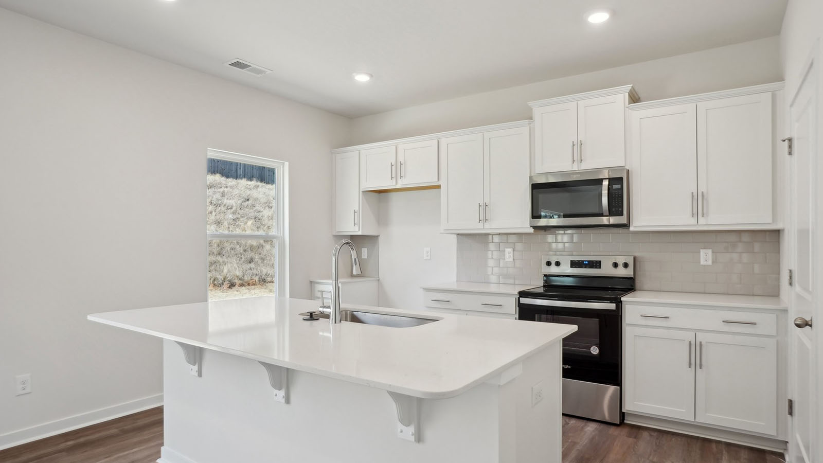 kitchen and island with white cabinets, wood floors and stainless steel appliances