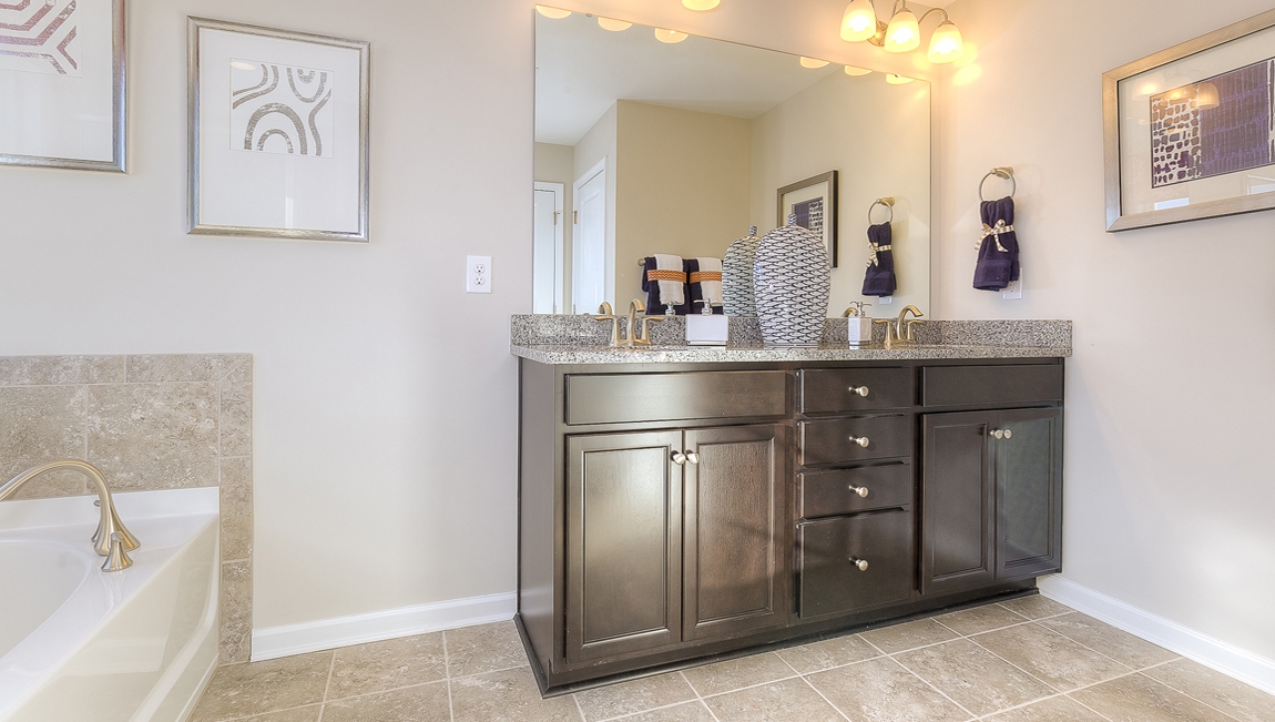 Primary bathroom with double sinks, brown cabinets and bathtub and glass door shower combination