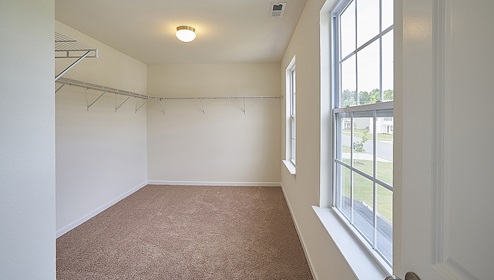 Carpeted primary walk in closet with window