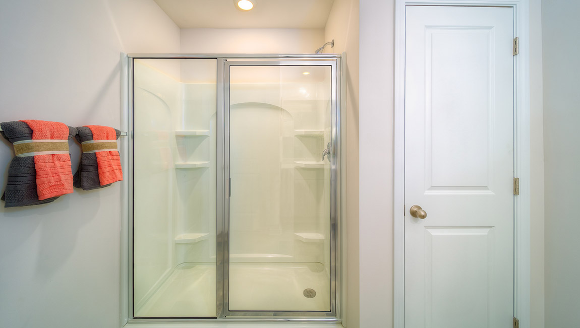 Primary bathroom with white counters and cabinets, double sinks and glass door shower