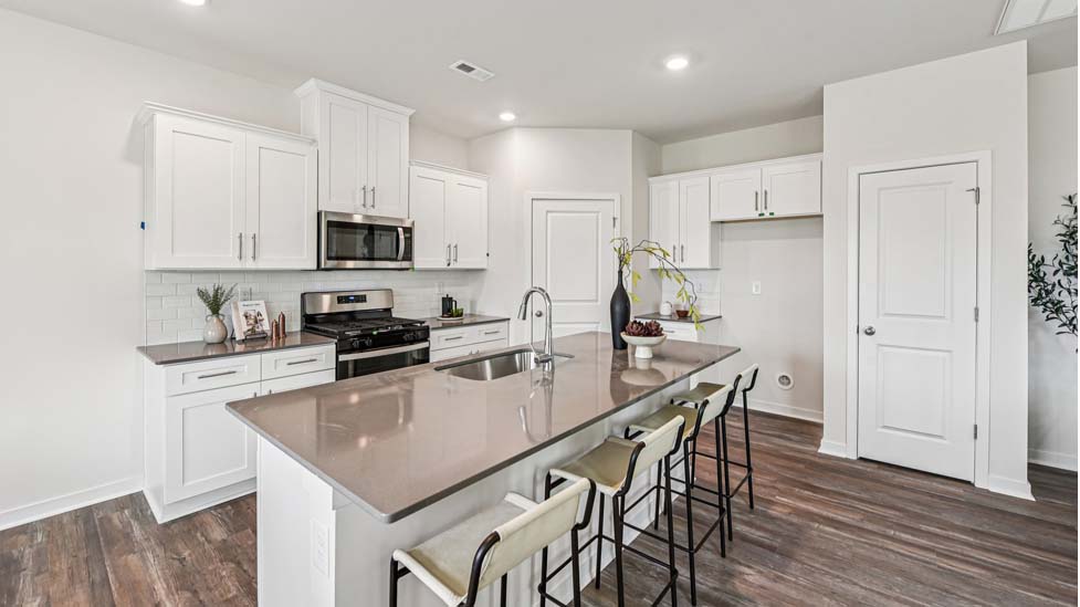 Kitchen and island with white cabinets, quartz counters, wood floors and stainless steel appliances
