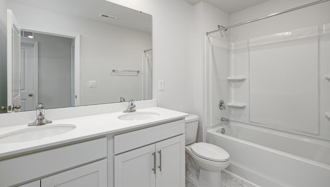 Bathroom with double sinks, white cabinets and counters, and bathtub