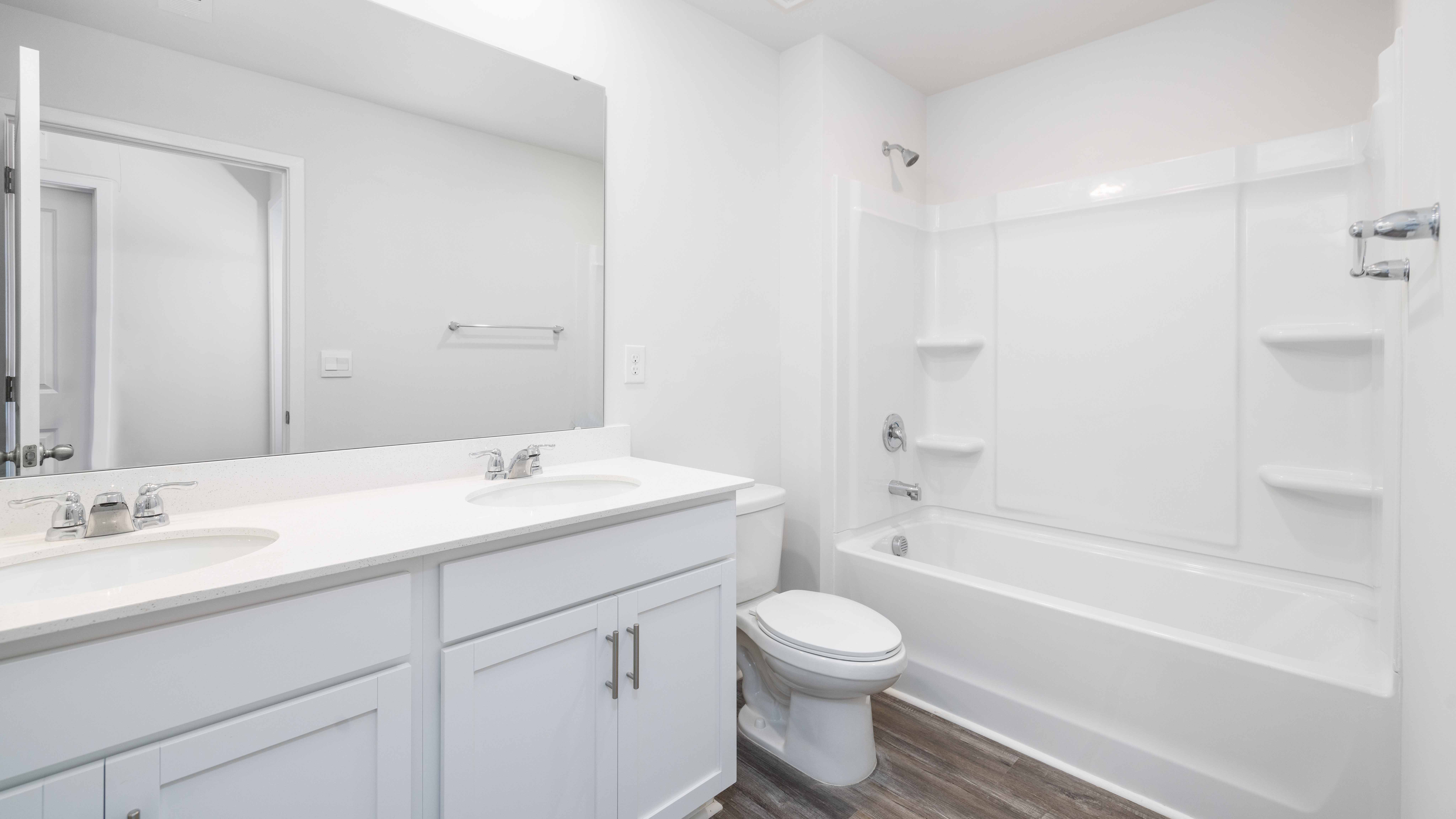 Bathroom with double sinks, white cabinets and counters, and bathtub