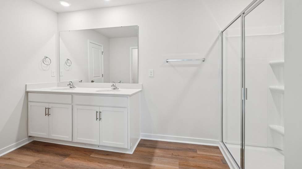Primary bathroom with double sinks, white cabinets and glass door shower
