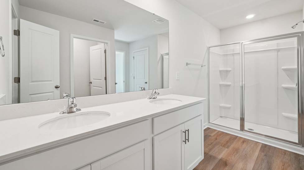 Primary bathroom with double sinks, white cabinets and glass door shower