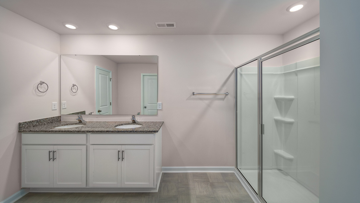 Primary bathroom with double sinks, white cabinets and glass door shower