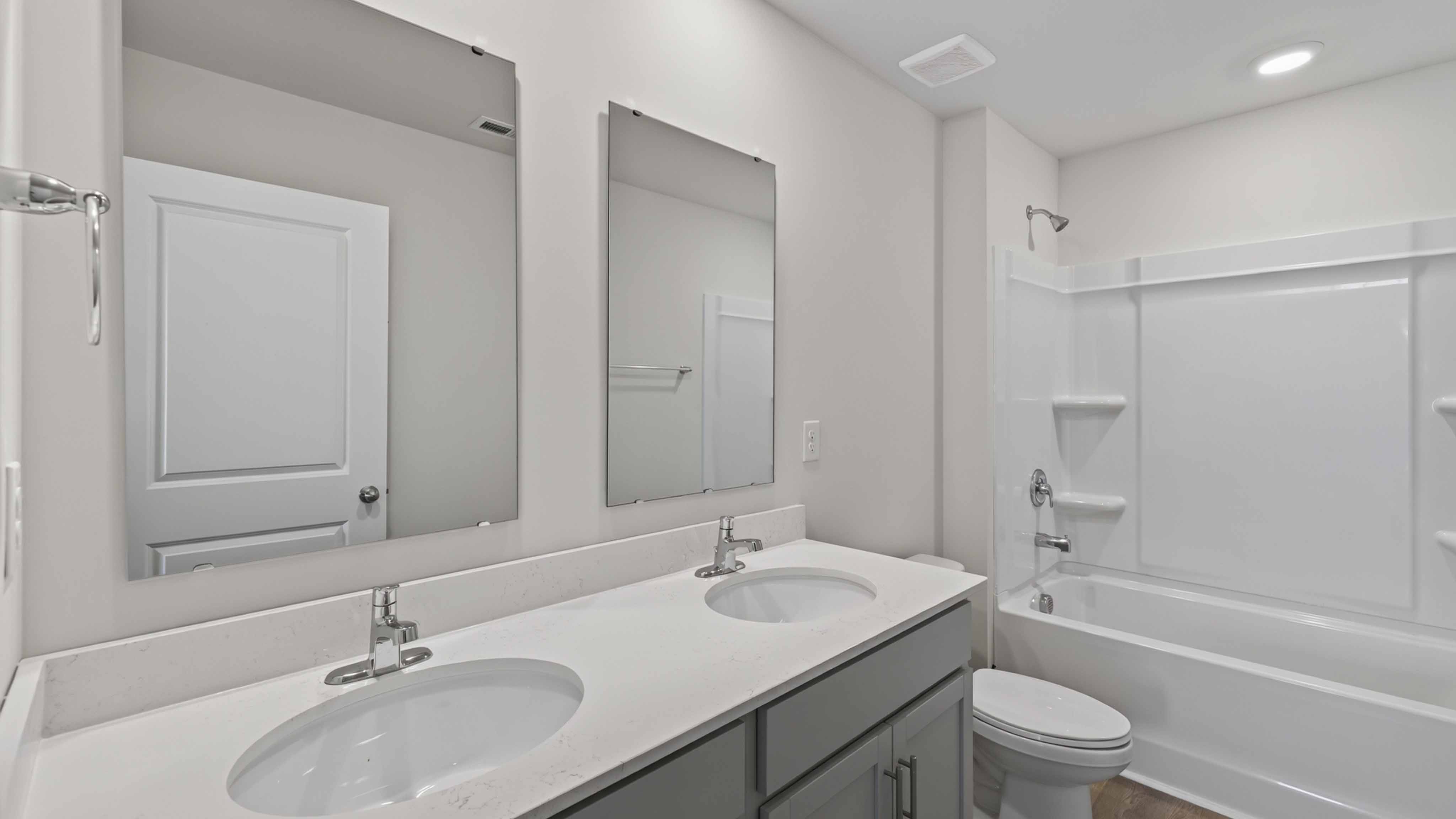 Bathroom with bathtub, double sinks, and white counters and cabinets