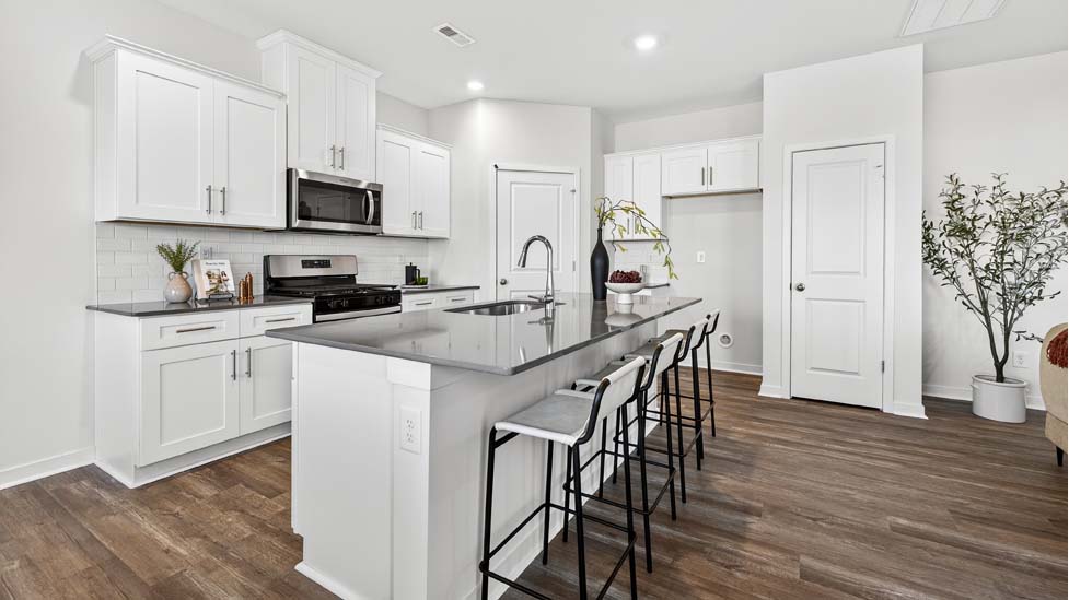 Kitchen and island with white cabinets, quartz counters, wood floors and stainless steel appliances