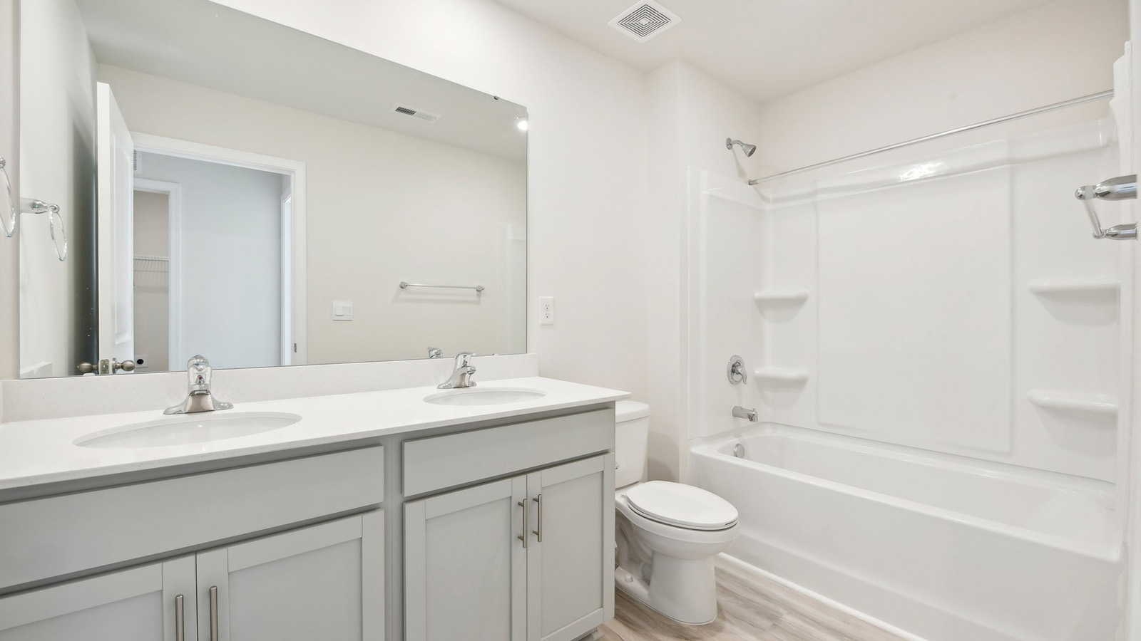 Bathroom with double sinks, white cabinets and counters, and bathtub
