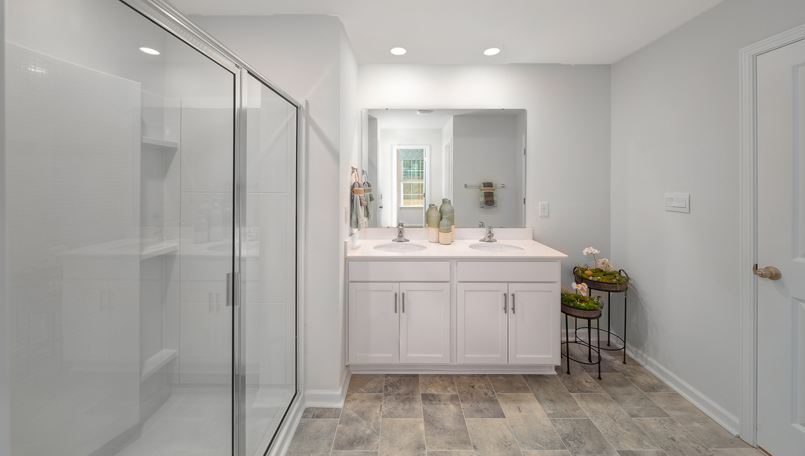 Primary bathroom with double sinks, white counters, and cabinets, glass door shower