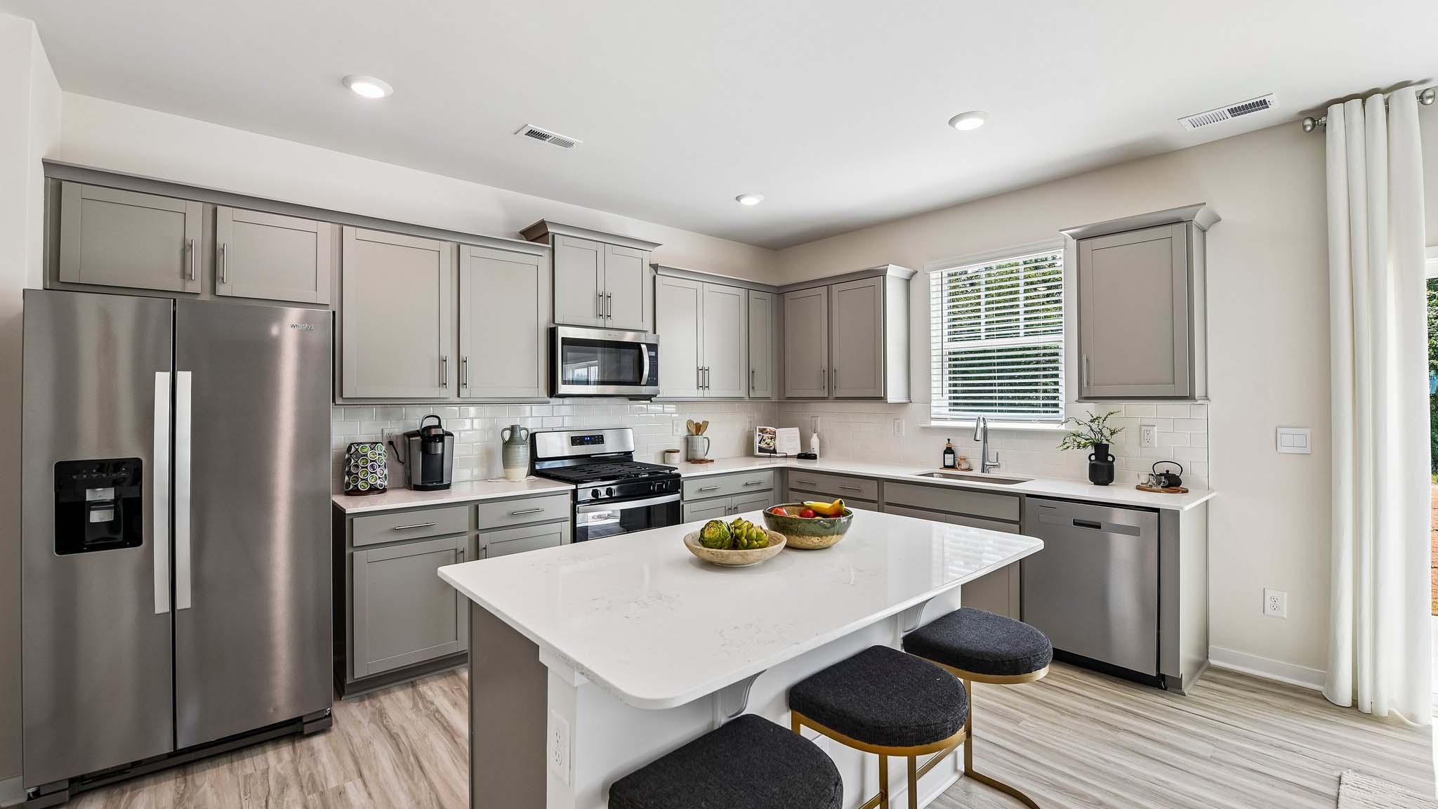 Kitchen and island with white cabinets, quartz counters, wood floors and stainless steel appliances