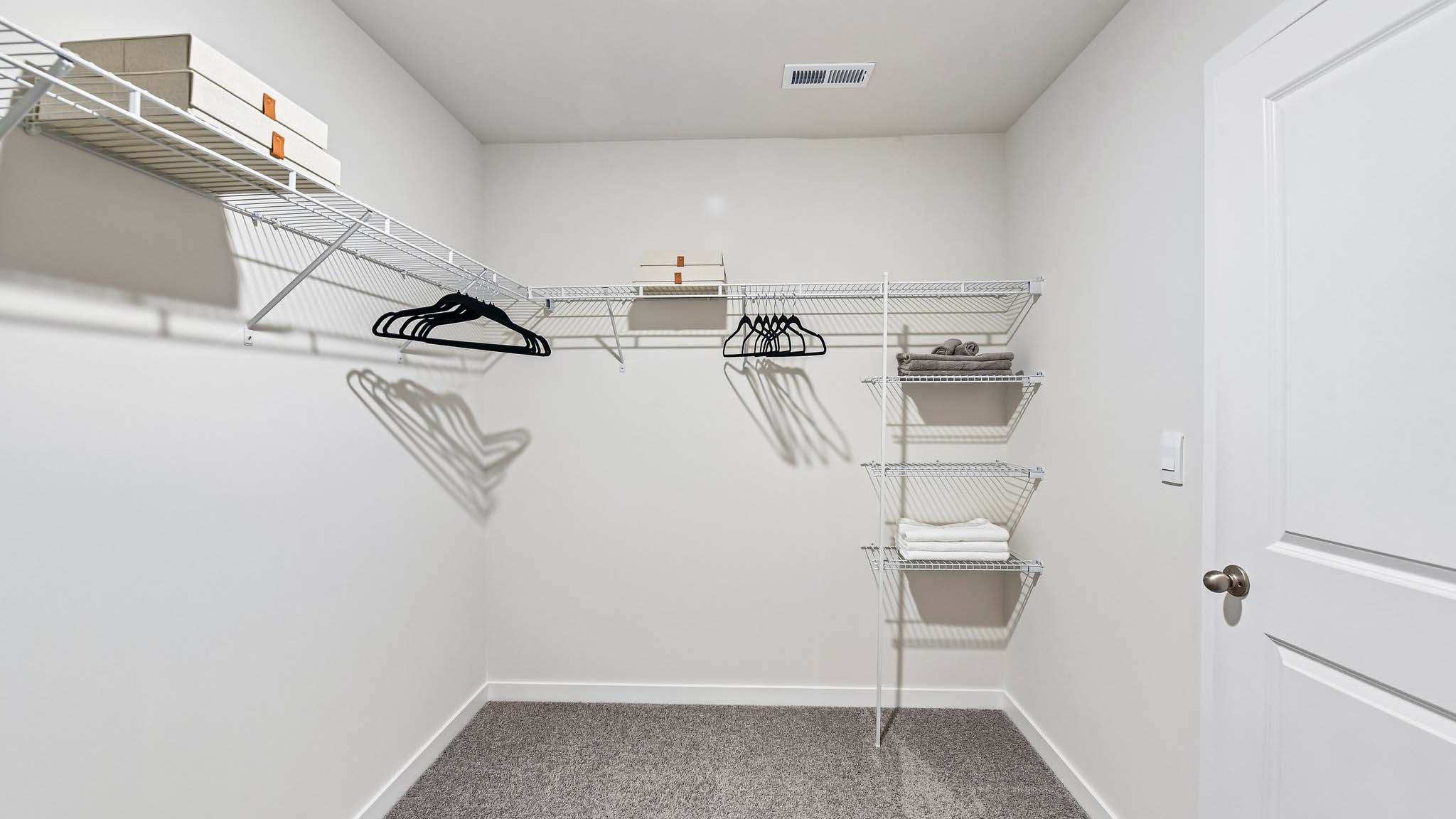 Primary carpeted walk in closet with built in racks for hanging