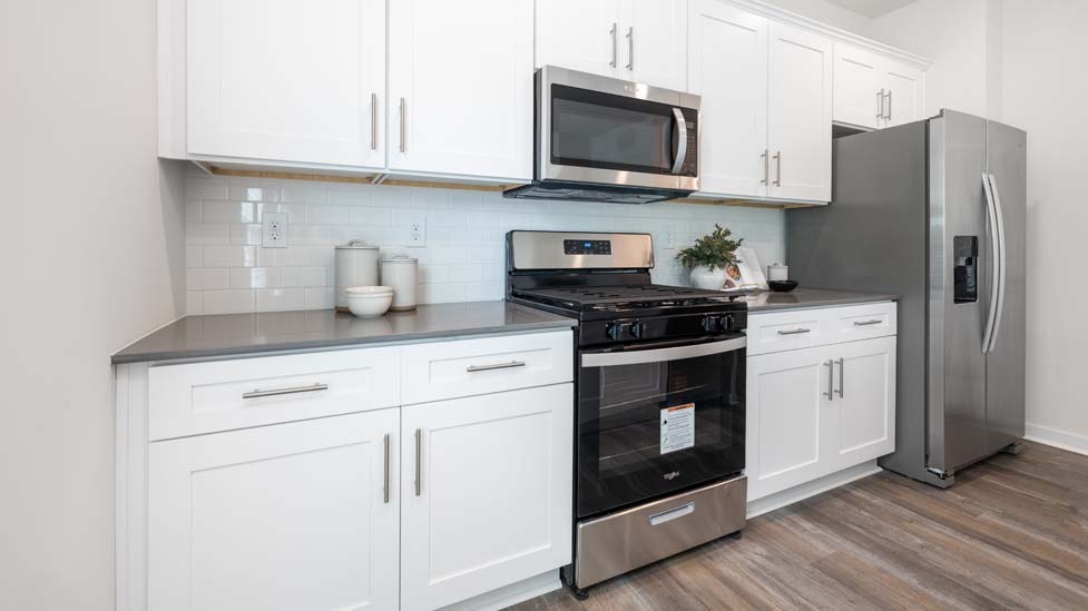 Kitchen and island with white cabinets and counters, vinyl floors and stainless steel appliances